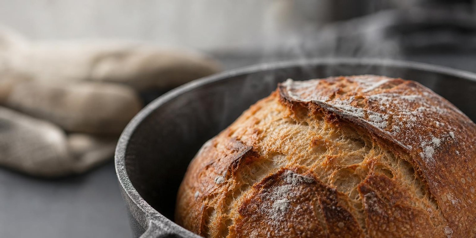 Frisch gebackener Brotlaib mit aufgerissener Kruste dampft im gusseisernen Topf.