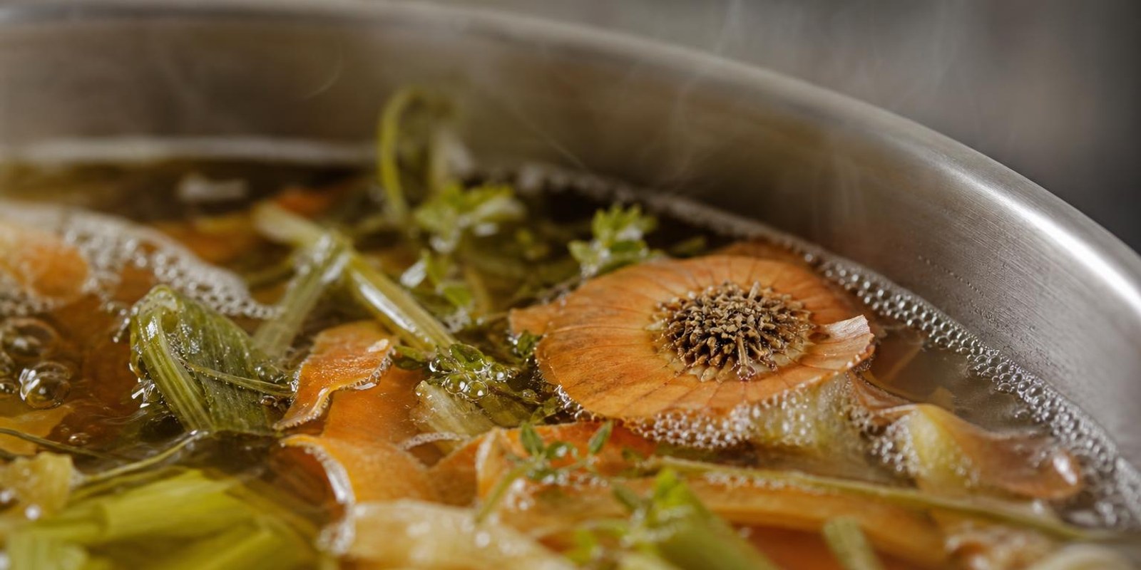 Zwiebelenden, Karottenschalen und Lauchgruen ziehen in einem Topf zu goldener Gemuesebruehe.