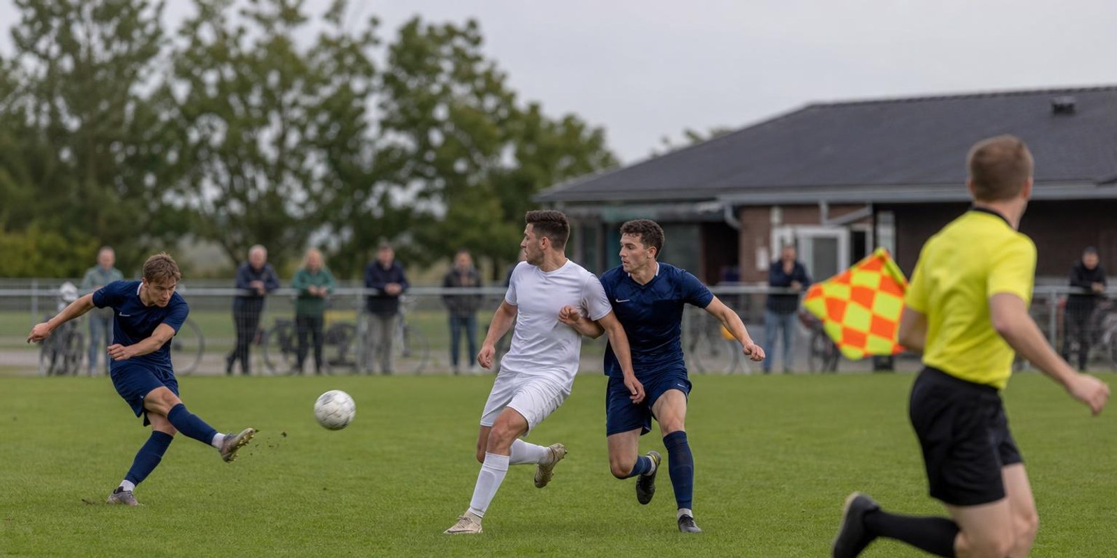 Stuermer und letzter Verteidiger sprinten beim Abspiel auf gleicher Hoehe, der Linienrichter beobachtet.