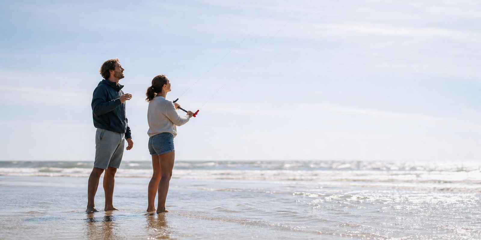 Kite-Anfaenger uebt mit Trainerkite am Strand, der Lehrer steht direkt dahinter.