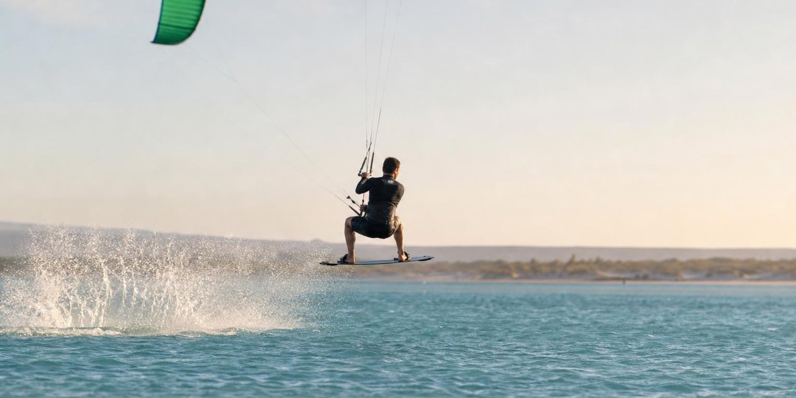 Kiter schwebt bei seinem ersten kontrollierten Sprung knapp ueber dem flachen Wasser.