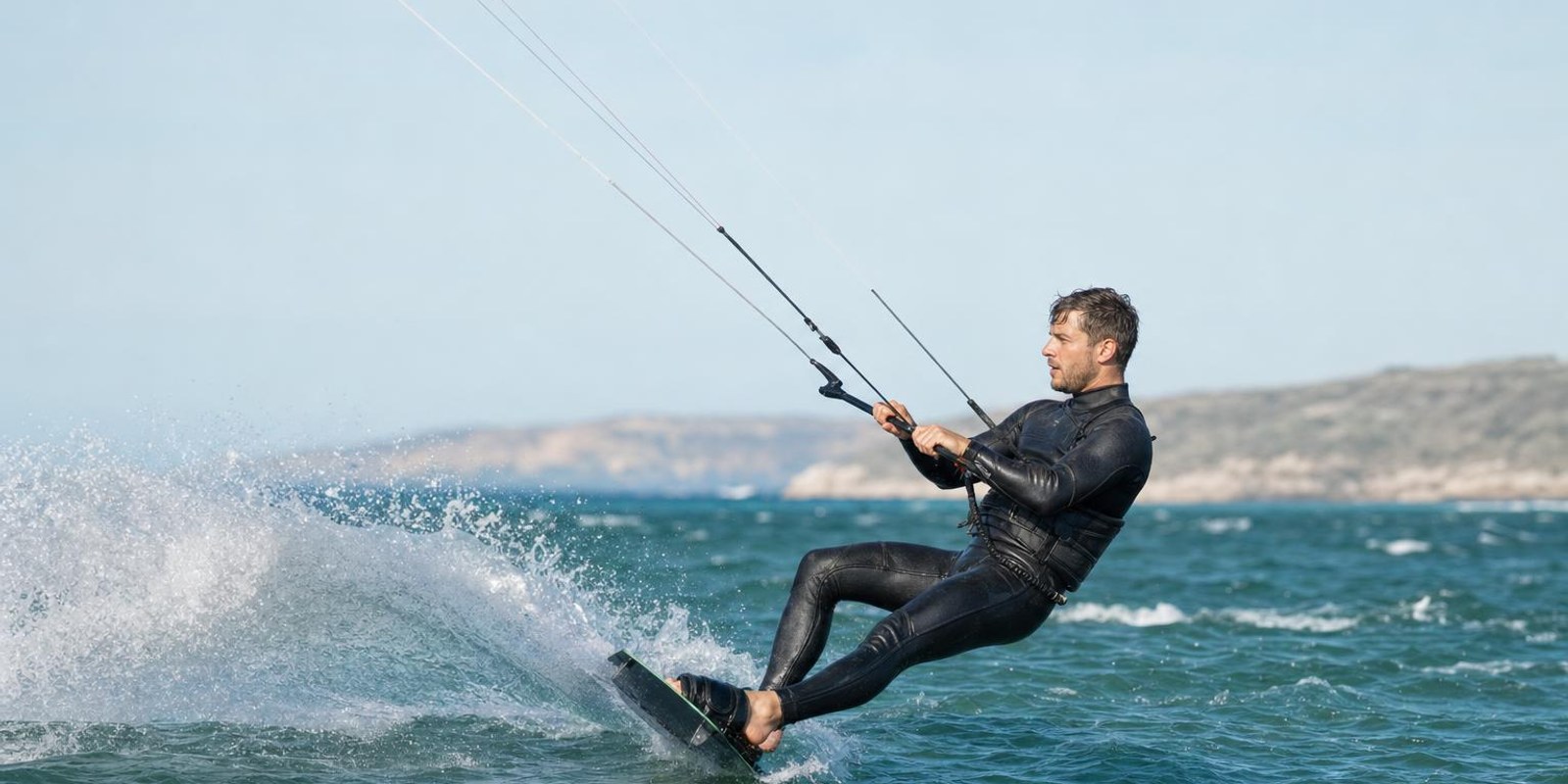 Ein Kitesurfer richtet sich beim Wasserstart aus dem Wasser auf, waehrend der Kite ihn nach vorn zieht.