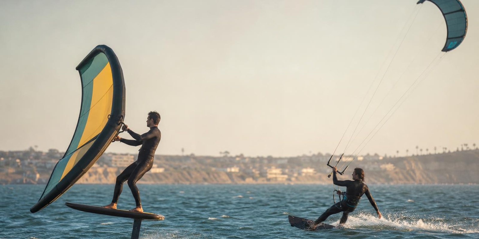 Wingfoiler und Kitesurfer fahren auf demselben Revier nebeneinander uebers Wasser.