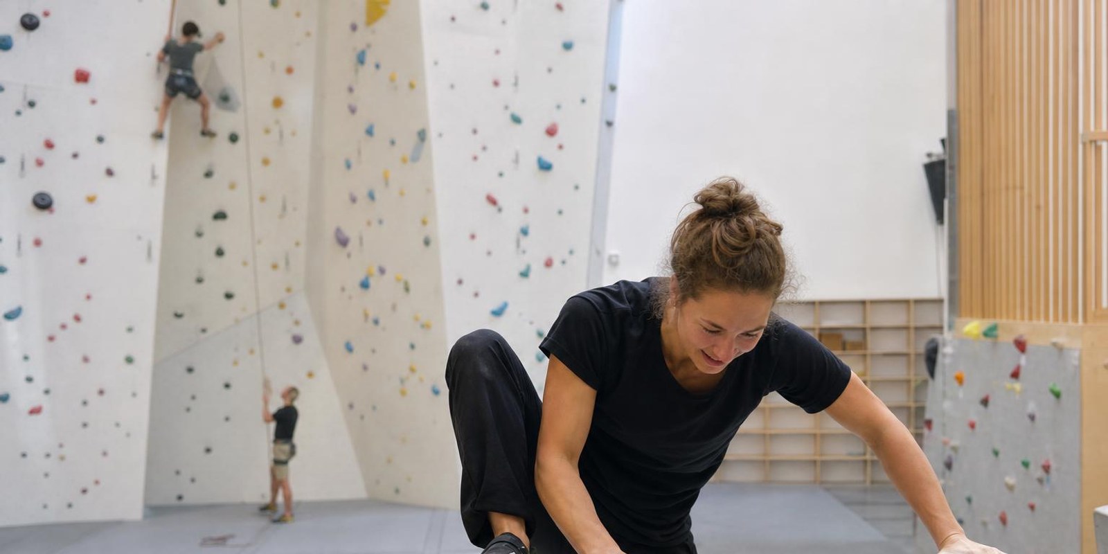 Vorn klettert ein Boulderer ueber Matten, hinten haengt ein Seilkletterer hoch in der Wand.