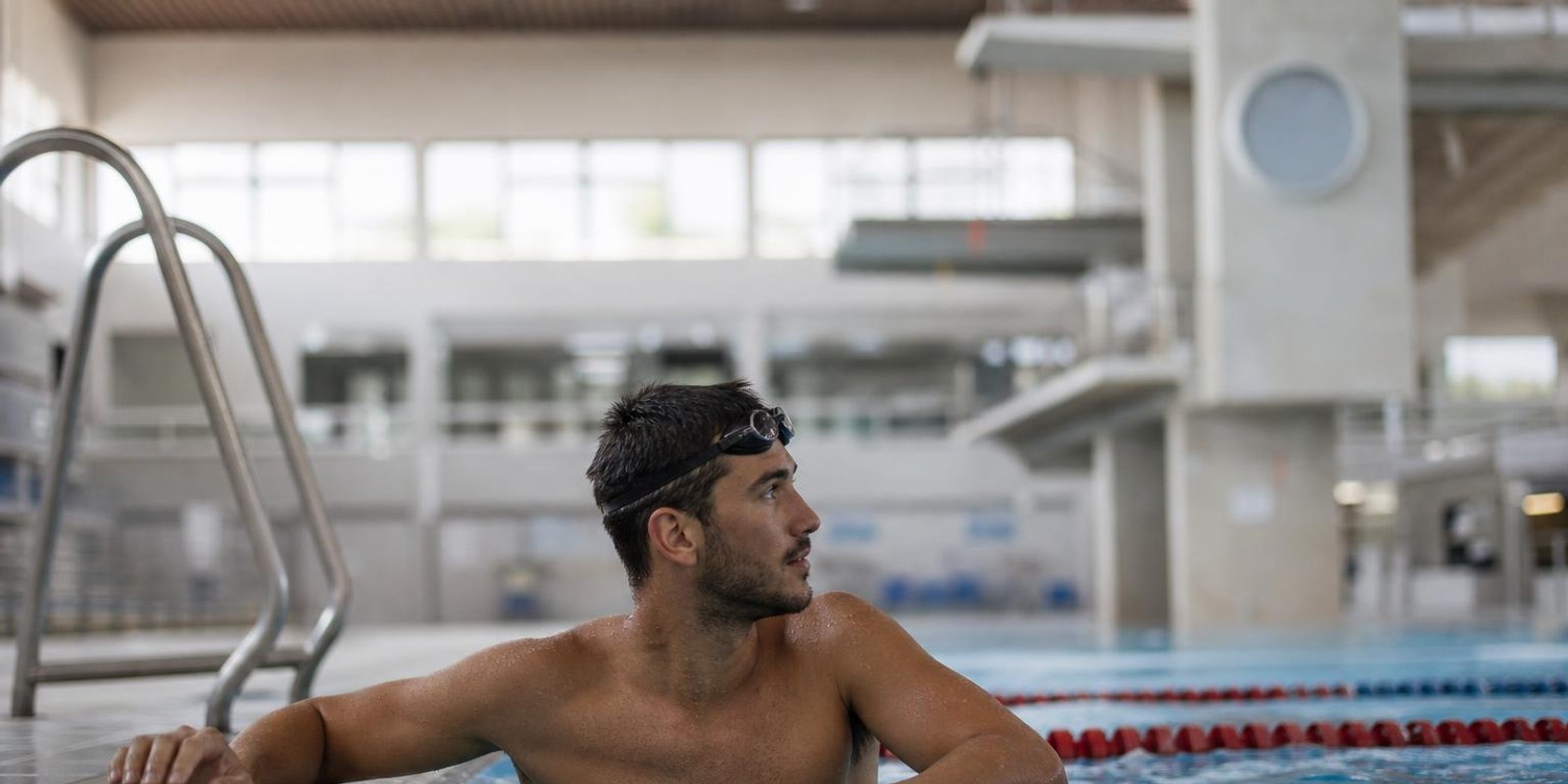 Schwimmer haengt zwischen zwei Serien am Beckenrand und blickt zur Tempouhr.