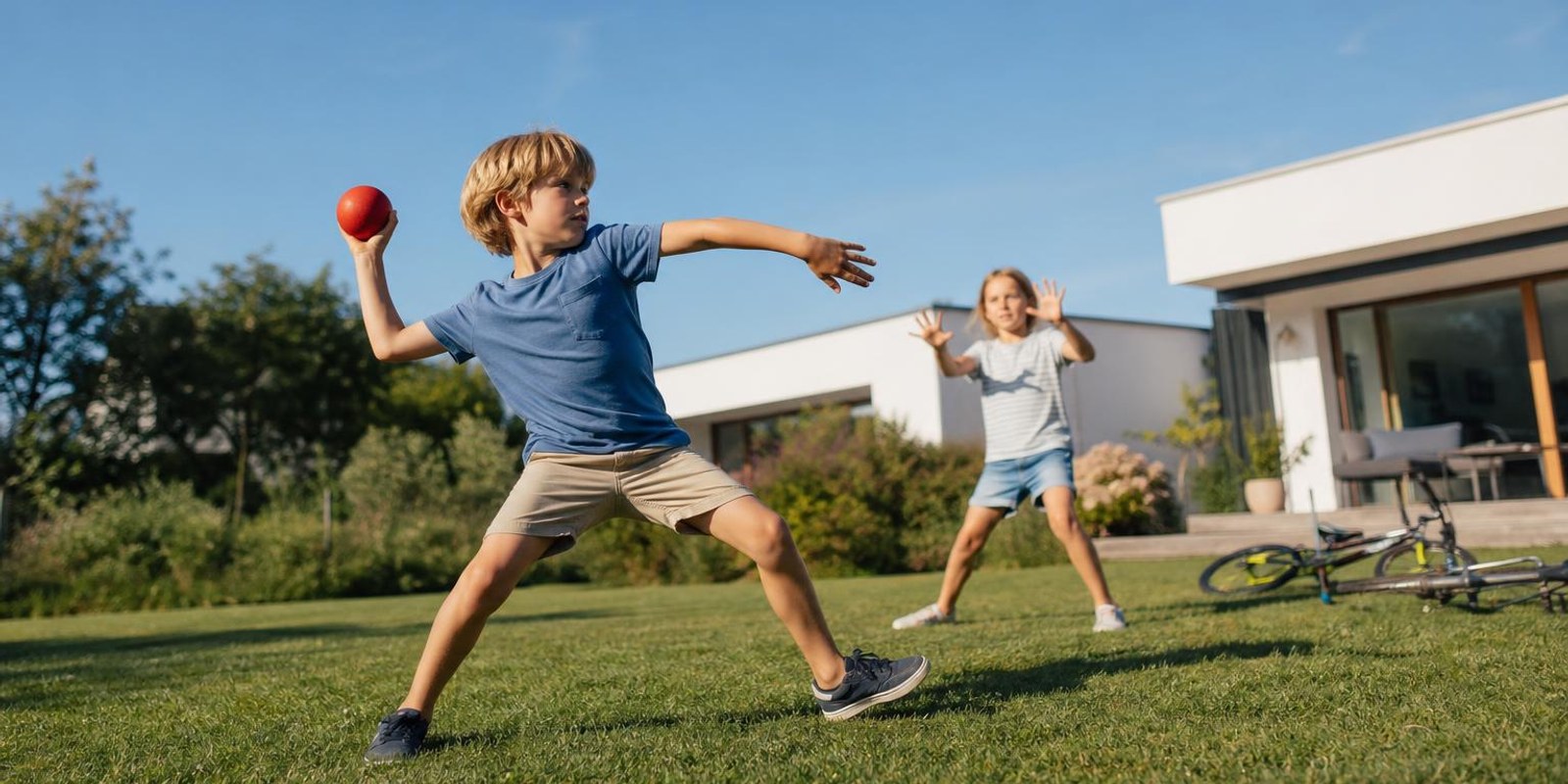 Kinder spielen bei hellem Tageslicht draussen im Garten und schauen dabei in die Ferne.
