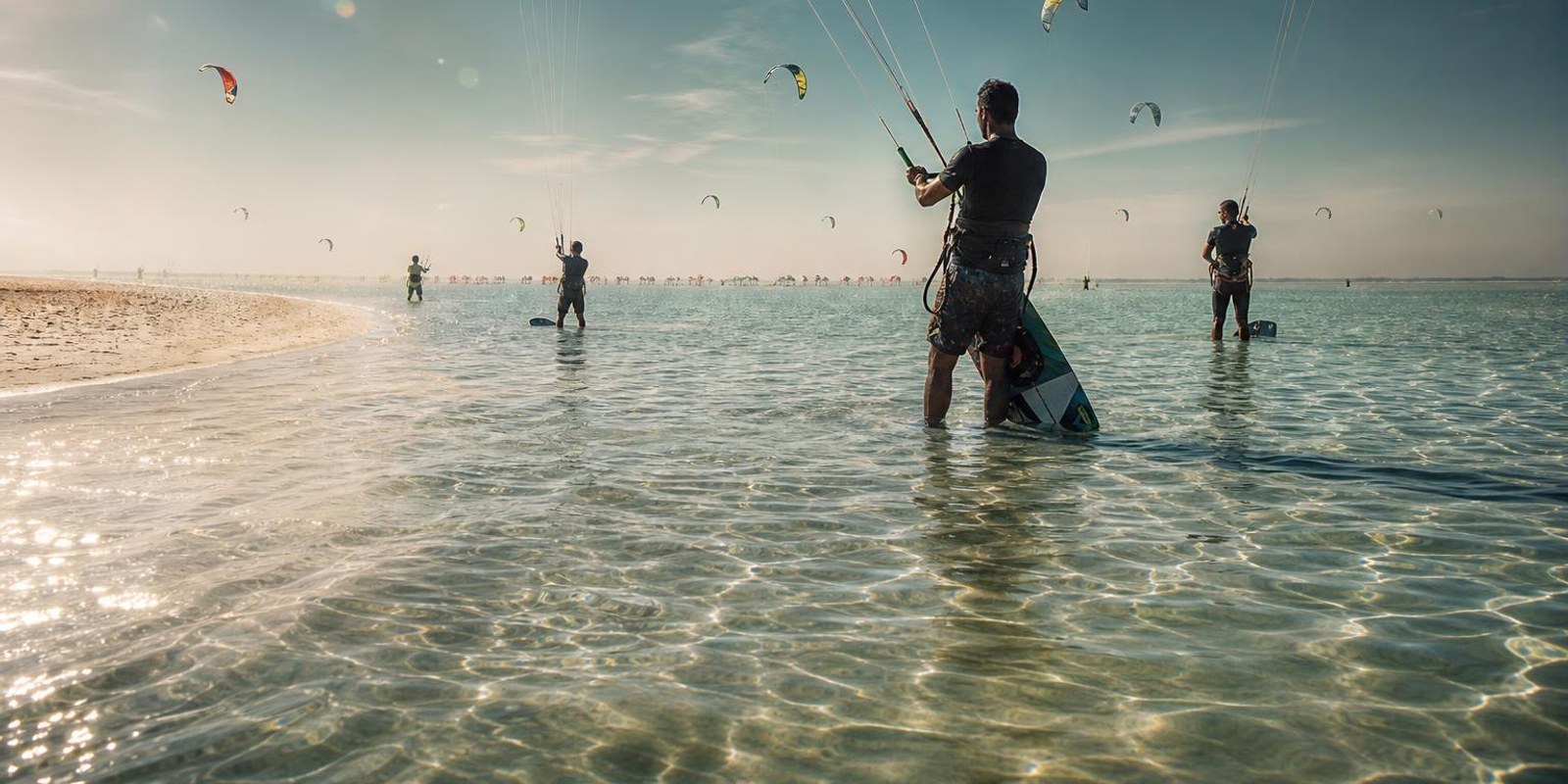 Flache Lagune mit heller Sandzunge vor Djerba, viele bunte Kites stehen im Thermikwind.