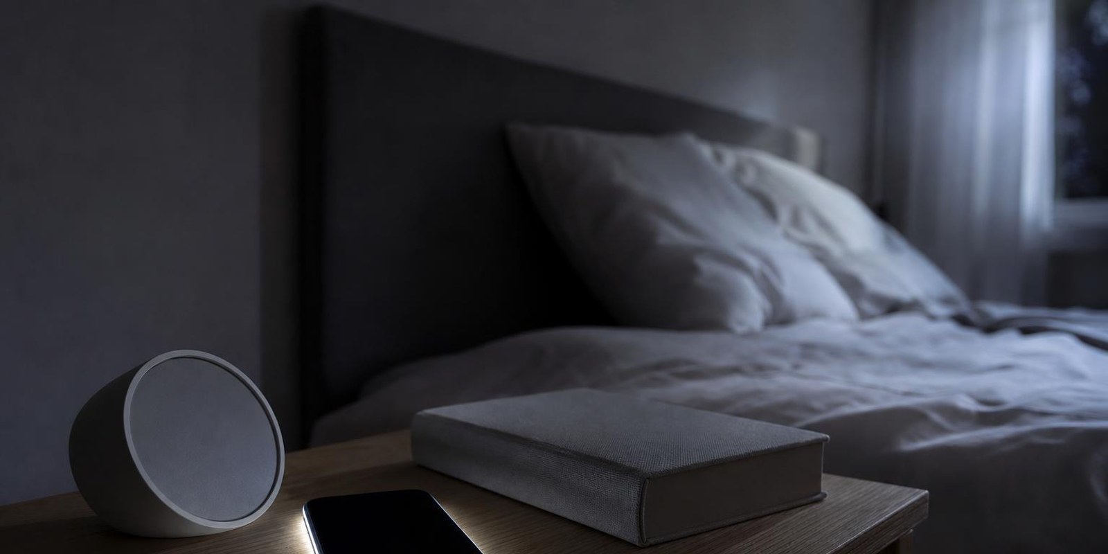 Smartphone laedt nachts am Kabel auf dem Nachttisch neben Wecker und Buch.